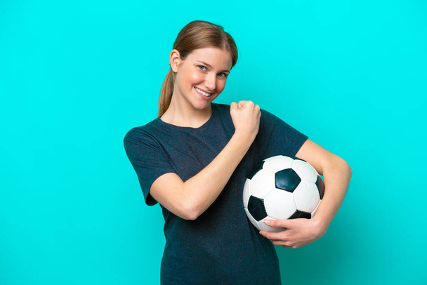 Молода жінка-футболістка ізольована на синьому фоні, відзначаючи перемогу
 - Фото, зображення