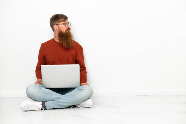 Giovane uomo caucasico rossastro con computer portatile isolato su sfondo bianco guardando di lato - Foto, immagini