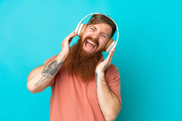 Young reddish caucasian man isolated on blue background listening music - Foto, afbeelding
