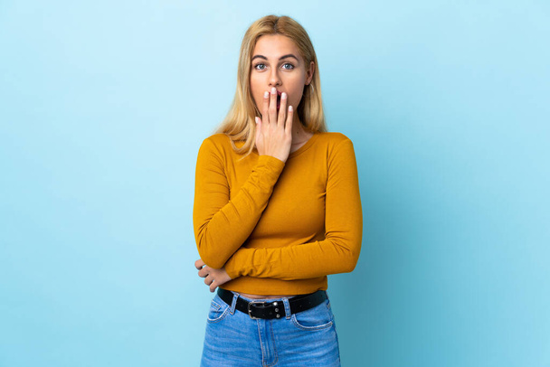 Junge uruguayische blonde Frau vor isoliertem blauen Hintergrund überrascht und schockiert, während sie nach rechts schaut - Foto, Bild