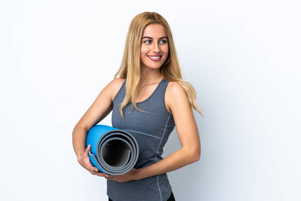 Молода спортивна жінка ходить на заняття з йоги, тримаючи килимок над ізольованим білим тлом
 - Фото, зображення