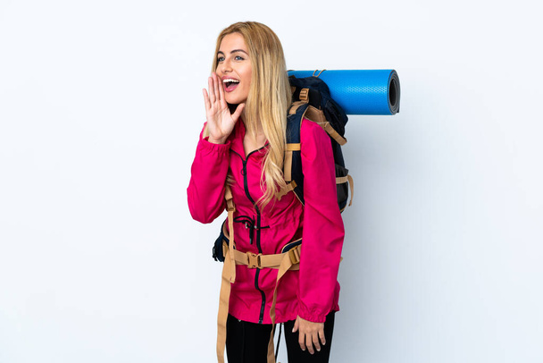 Mujer joven montañista con una gran mochila sobre fondo blanco aislado gritando con la boca abierta - Foto, imagen