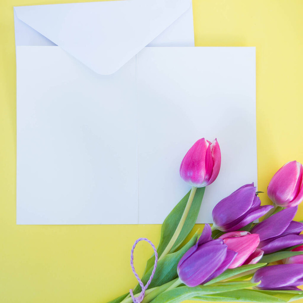 white card and envelope on yellow ground with pink tulips with space for text - Photo, Image