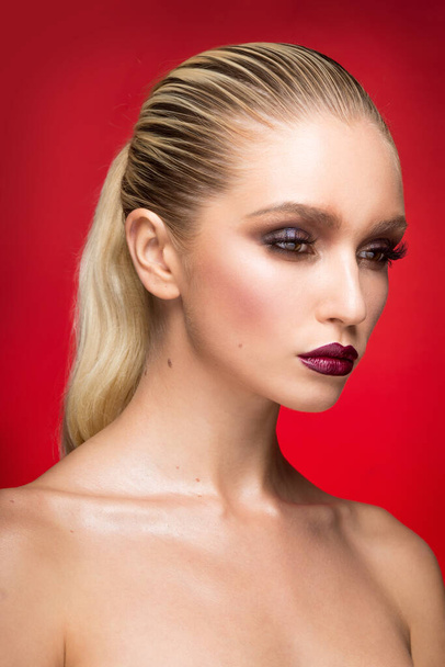Close-up portret van jonge vrouw model met perfecte make-up met blote schouders, geïsoleerd op een rode achtergrond. - Foto, afbeelding