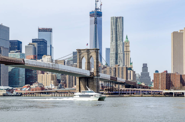 Brooklyn Bridge New York City with construction area on the bridge with Manhattan Skyline and One World Trade Center Construction area in the Background, Hudson river with seastreak ship passing by in the forefront, daytime with great weather - Zdjęcie, obraz