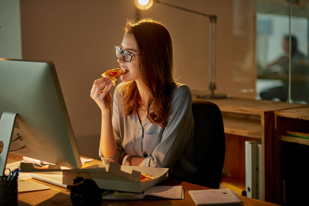 Pranzi notturni in ufficio. Girato di una giovane donna d'affari attraente che mangia pizza mentre lavora fino a tardi in ufficio. - Foto, immagini