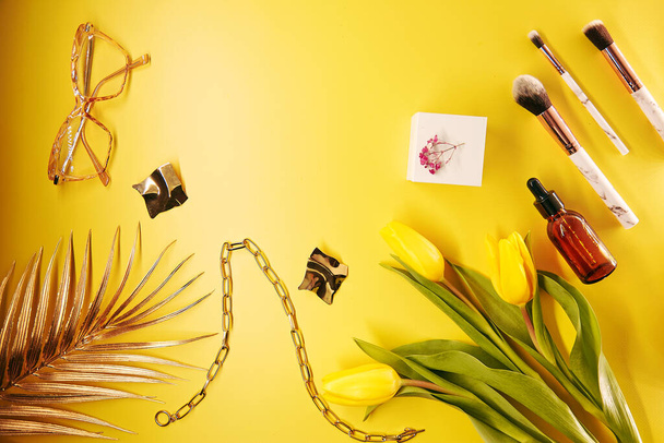 Cosmetici alla moda, accessori, pennelli per il trucco e accessori su sfondo giallo. Foglie di palma, tulipani, bicchieri, contagocce siero, decorazioni. Ricevuto. Foto di alta qualità - Foto, immagini