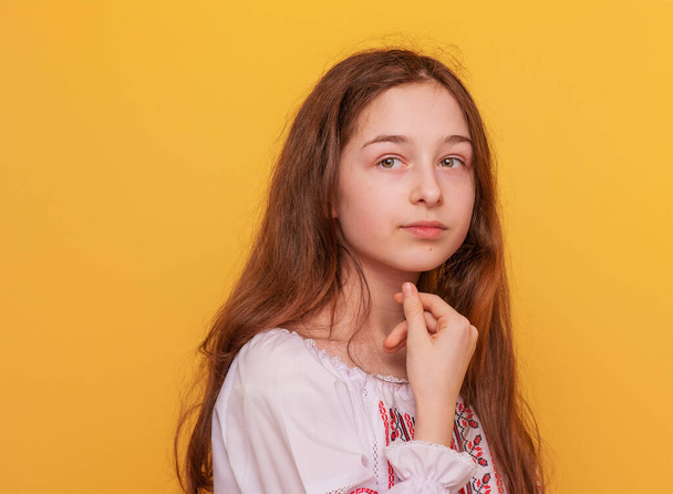 Portret van een 11-jarig meisje in Oekraïense geborduurde kleren. Meisje op een gele achtergrond. - Foto, afbeelding