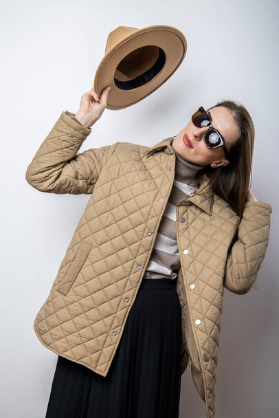 A young woman in a jacket takes off her hat near a white wall - Photo, image