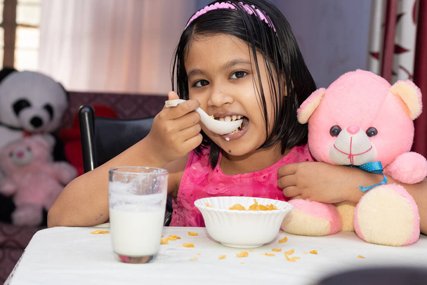 Una bambina indiana mangia cereali con latte dal viso sorridente e guarda la macchina fotografica - Foto, immagini
