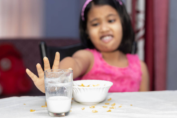 Focus selettivo su una bambina indiana con farina incompleta di cornflakes e latte che mostra antipatia - Foto, immagini
