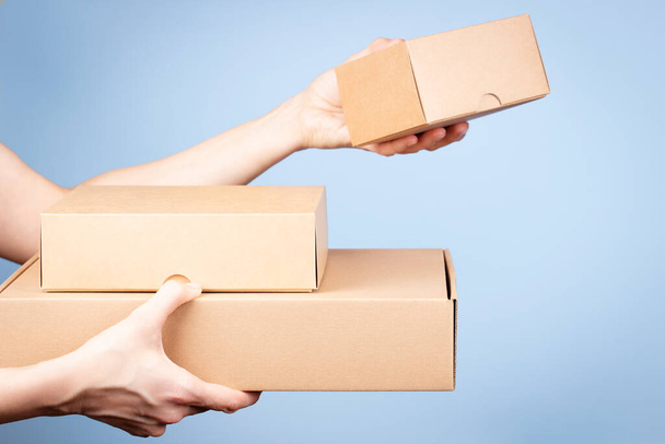 Stack of cardboard boxes in female hands. Blank parcel boxes on light blue background. Packaging, shopping, free shipping, delivery concept - Foto, Bild