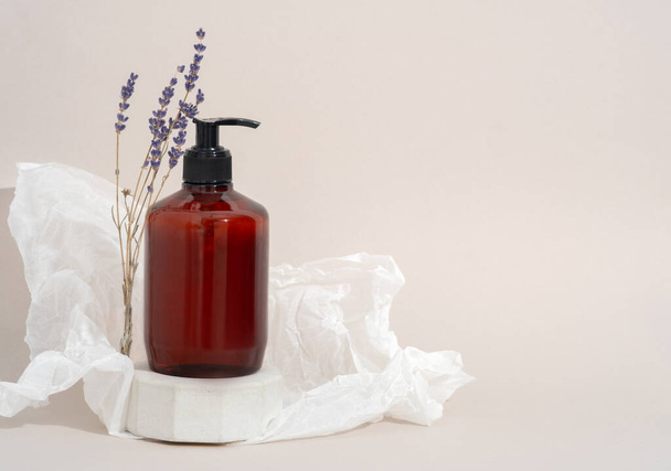 Mockup Spa body cosmetics in brown bottles gel, shower soap, shampoo with a pump on a concrete podium stand with lavender branches on a beige background and crumpled paper decoration. - Photo, Image