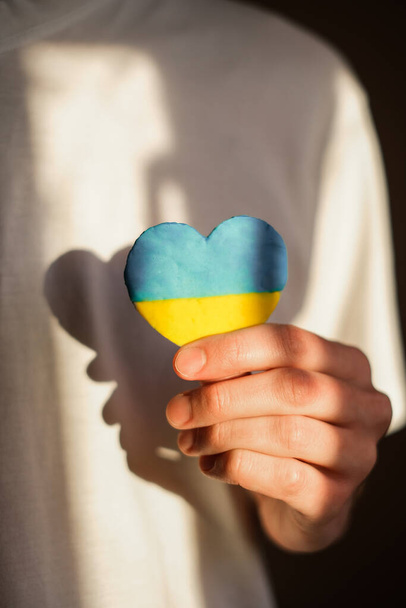 un hombre con una camiseta blanca sostiene un corazón con la bandera de Ucrania. guerra en Ucrania - Foto, Imagen