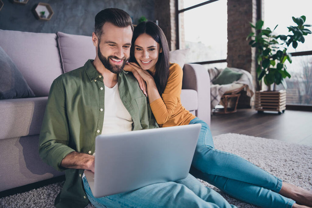Portrait of beautiful handsome cheerful couple sitting on floor using laptop searching tour at home house flat indoors - Photo, image