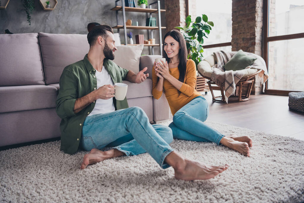 Portrait of attractive cute cheerful couple sitting on floor carpet communicating spending day drinking cacao at home house flat indoors - Fotografie, Obrázek