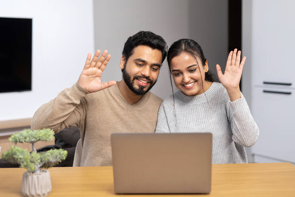 Multiracial man and woman waving hello into webcam, smiling and greeting. Interracial couple talking online, having video meeting on the laptop with family or friends - Photo, Image