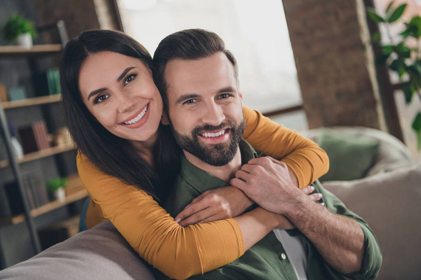 Portrait of attractive cheerful couple hugging spending vacation sitting on sofa having fun at home house flat indoors - Fotó, kép