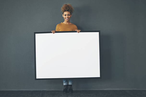 Anunciaré tu mensaje. Retrato de estudio de una mujer joven sosteniendo un cartel en blanco sobre un fondo gris. - Foto, imagen