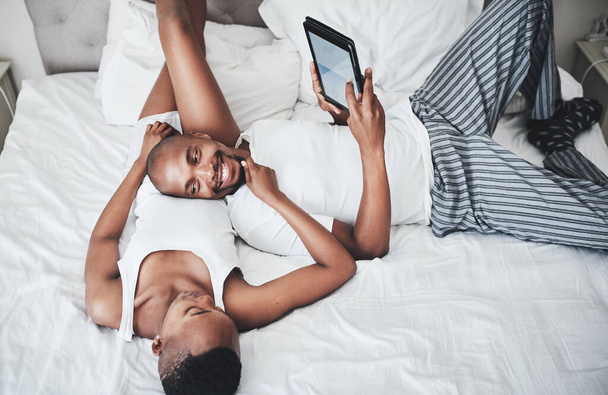 Leniwe dni są jeszcze lepsze, kiedy są dzielone. Zdjęcie szczęśliwej młodej pary korzystającej z tabletu cyfrowego w sypialni w domu. - Zdjęcie, obraz