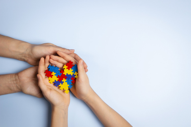 Koncept Světového dne autismu. Dospělé a dětské ruce drží puzzle srdce na světle modrém pozadí. Horní pohled - Fotografie, Obrázek