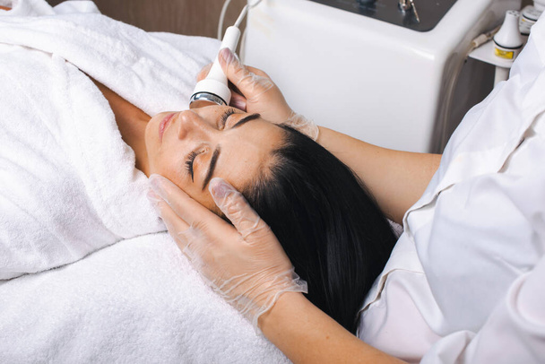 Mulher caucasiana deitada em uma mesa recebendo tratamento de cavitação facial no salão de spa. Estilo de vida saudável. Tratamento facial. Jovem mulher cuidados com a pele. Facial - Foto, Imagem