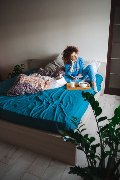Curly girl sitting in bed looking out the window thoughtfully before eating her healthy breakfast. Healthy lifestyle. Healthy food, diet. Fresh healthy food. - Foto, imagen
