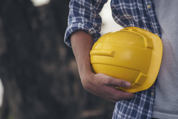 Mérnök férfi kezek kezében keménykalap fehér munka sisak kemény kalap Építőmérnöki. Építőmérnök férfi biztonsági ruhában tartsa fehér munka sisak kemény kalap a kezét az építési területen - Fotó, kép