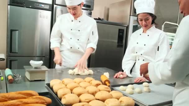 Profesionální gurmánský tým, tři mladí kuchaři v bílých kuchařských uniformách a zástěrách hnětou těsto a vejce, připravují chléb a čerstvé pečivo, pečou v troubě v kuchyni restaurace z nerezové oceli. - Záběry, video