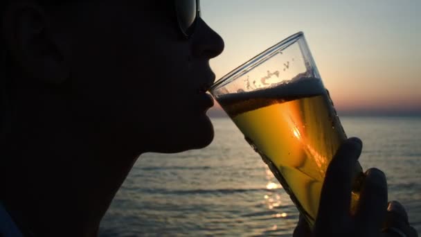 Kobieta pije piwo na plaży o zachodzie słońca - Materiał filmowy, wideo
