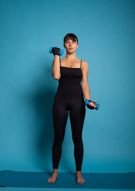 Retrato de una mujer en forma que sostiene pesas esparciendo músculos corporales - Foto, imagen