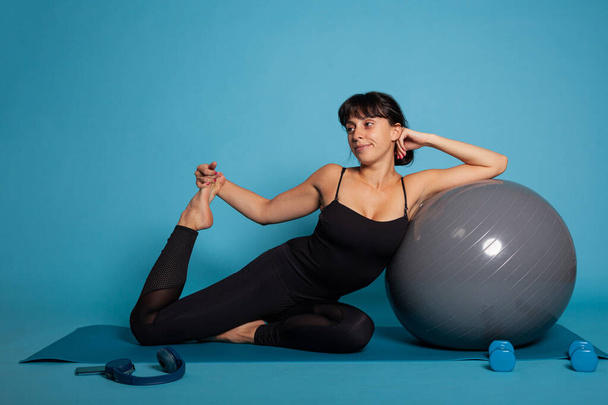 Portrait of athlete woman sitting on yoga mat leaning on yoga fitball - Photo, Image