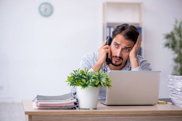 Jonge mannelijke werknemer ongelukkig met overmatig werk in het kantoor - Foto, afbeelding