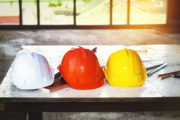 Безопасная рабочая концепция: защитные шлемы, собранные вместе: белые, оранжевые и желтые шляпы аккуратно расставлены на столе на строительной площадке на высоком здании. - Фото, изображение