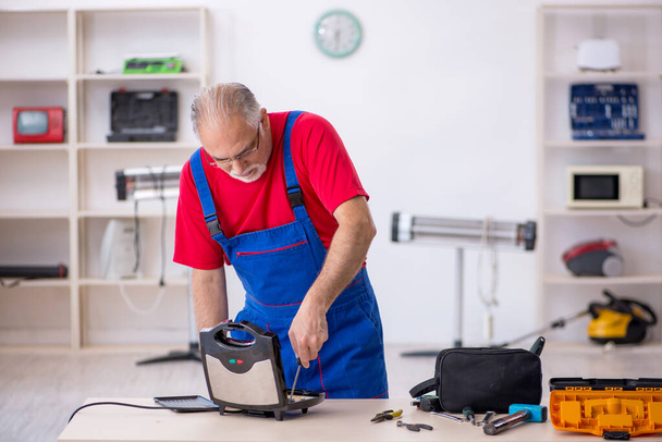Old repairman repairing sandwich maker at workshop - Foto, afbeelding