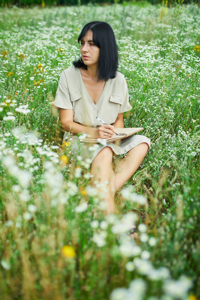 Nainen kynä kirjallisesti tai maalaus, käsiala muistikirja kukka kukkiva niitty, maaseudulla ulkona, alalla kesäpäivänä niityllä, tuntea luonto, rentoutua, yksin matkustaa. - Valokuva, kuva