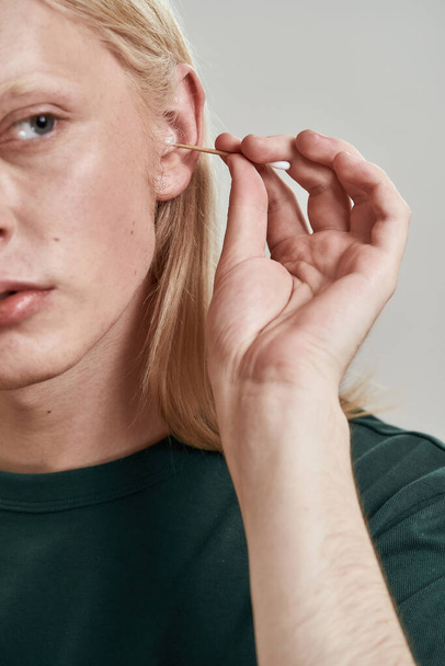 Cropped image of guy cleaning ear with ear stick - Fotó, kép