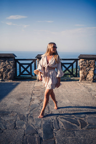 Eine junge Frau mit langen blonden Haaren in Top und Rock geht an einem sonnigen Sommertag spazieren. Glückliches Mädchen mit einem Lächeln im Gesicht und Sonnenbrille läuft an einem sonnigen Tag - Foto, Bild