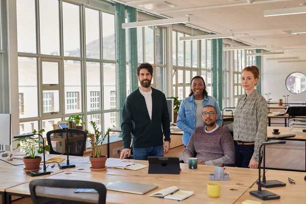 Confident group of diverse young businesspeople working together at a desk in modern open plan office space - Photo, image