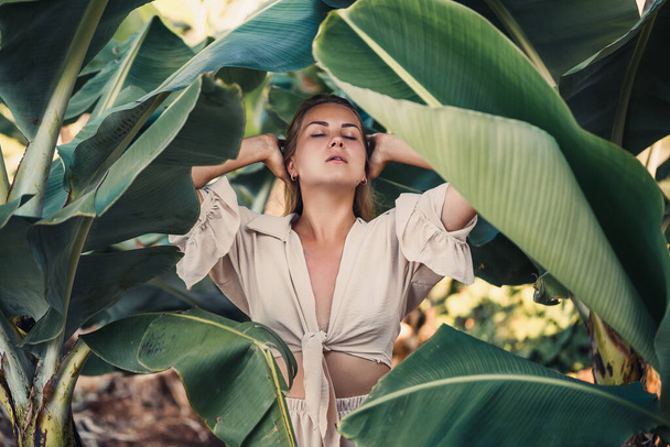 Beautiful woman in the jungle. A resort or hotel with tropical trees and plants. Woman with near banana leaf. Girl on vacation in the rainforest - Foto, imagen