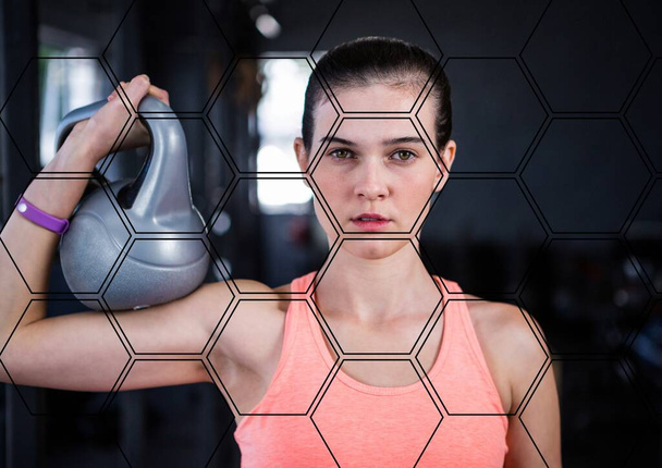 Hexagonal shapes pattern against portrait of caucasian fit woman holding a kettlebell at the gym. sports, fitness and technology concept - 写真・画像