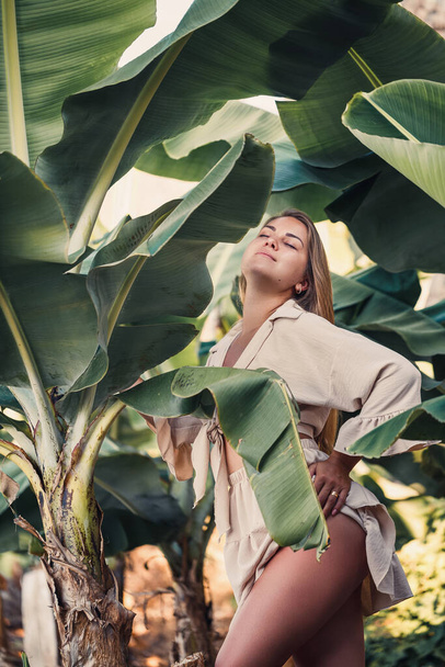 Schöne Frau im Dschungel. Ein Resort oder Hotel mit tropischen Bäumen und Pflanzen. Frau mit Beinahe-Bananenblatt. Mädchen im Urlaub im Regenwald - Foto, Bild