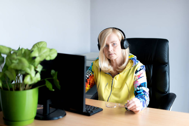 真剣に焦点を当てた中年女性の肖像｜オフィスコンピュータでウェブセミナーを見てヘッドフォンを身に着けています - 写真・画像