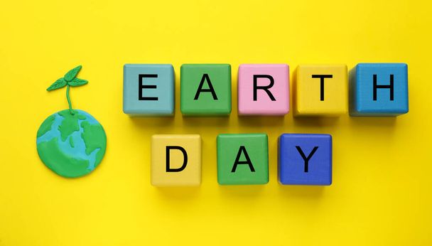Phrase Earth Day made with cubes and model of planet on yellow background, flat lay - Foto, Bild