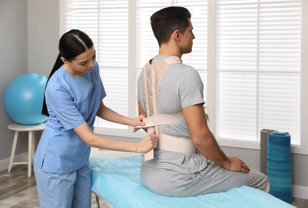 Orthopedist helping patient to put on posture corrector in clinic. Scoliosis treatment - Photo, image