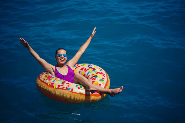 Młoda piękna dziewczyna w jasnym stroju kąpielowym leży na dużym nadmuchiwanym pierścieniu i unosi się na błękitnym morzu w słoneczny letni dzień - Zdjęcie, obraz