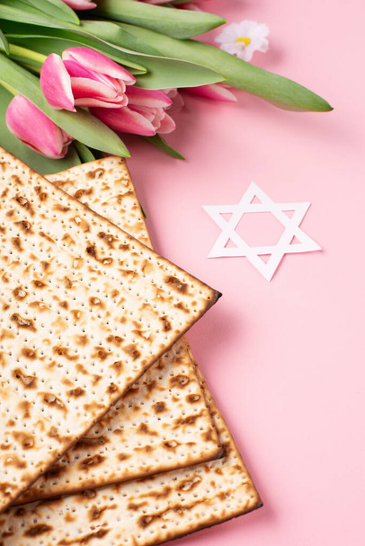 Jewish holiday Passover greeting card concept with matzah, nuts, tulip and daisy flowers on pink table. Seder Pesach spring holiday background, copy space. - Photo, Image