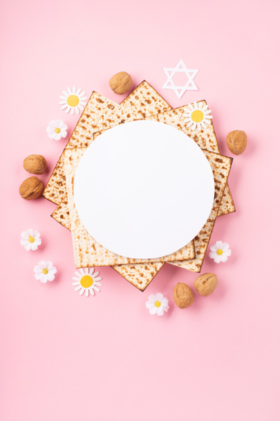 Jewish holiday Passover greeting card concept with matzah, nuts, tulip and daisy flowers on pink table. Seder Pesach spring holiday background, top view, copy space. - Photo, Image