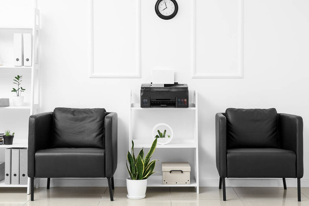 Kényelmes fotelek és polc egység modern nyomtatóval a fényfal közelében a szoba belsejében - Fotó, kép