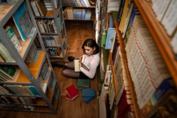 Güzel saçlı bir kız kütüphanede boş vakit geçirir. Kadın ve kütüphane kavramı - Fotoğraf, Görsel